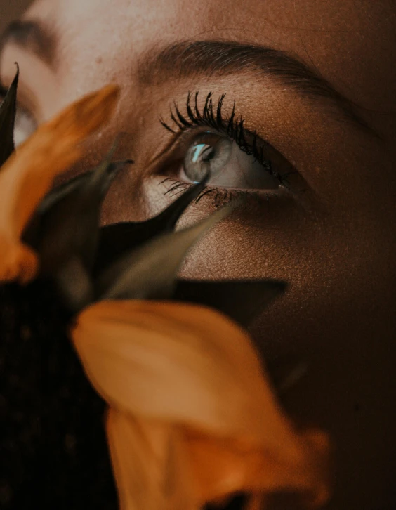 a woman holding a sunflower in front of her face, inspired by Elsa Bleda, trending on pexels, aestheticism, detailed eyes with pupils, orange and black tones, distant thoughtful look, low angle photo