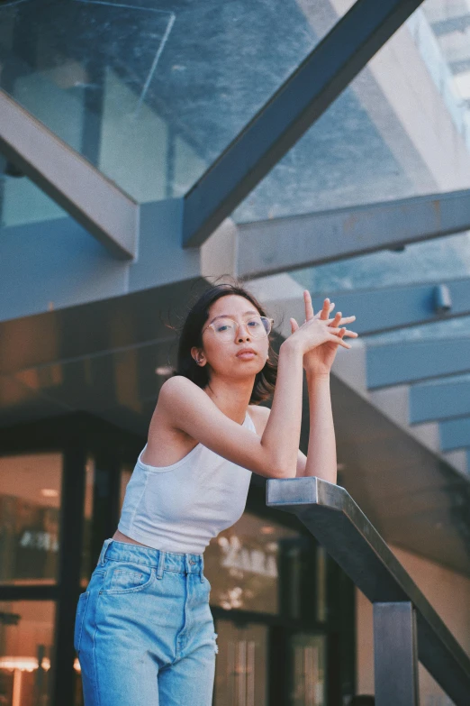 a woman standing on a set of stairs in front of a building, inspired by Feng Zhu, unsplash, realism, in a white tank top singing, pointing at the camera, young asian girl, denim