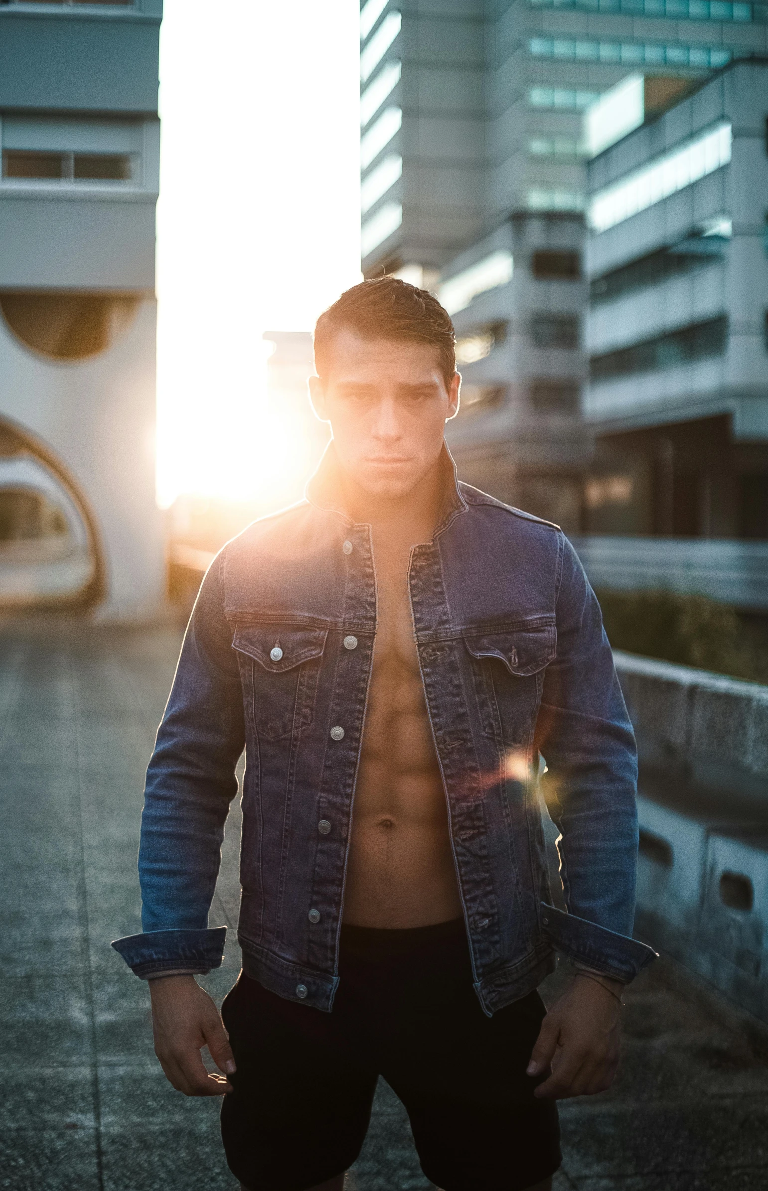 a shirtless man standing in front of a tall building, pexels contest winner, jean jacket, sun rising, professional modeling, casey cooke