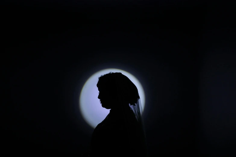 a silhouette of a person in the dark, an album cover, inspired by Carrie Mae Weems, unsplash, hurufiyya, circular white full moon, somali woman, halo of light, photographed for reuters