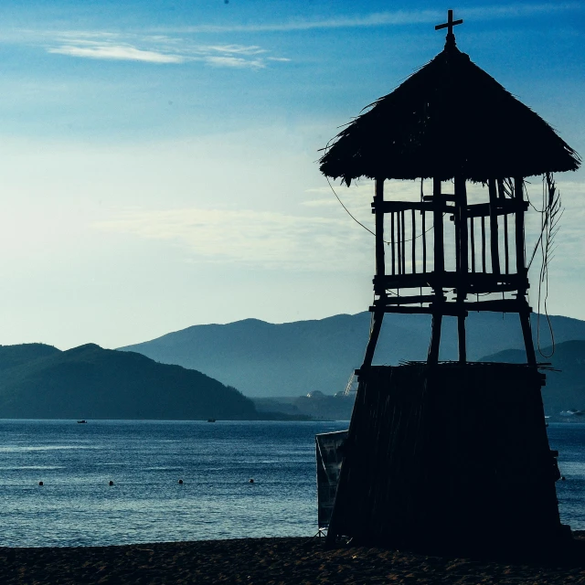 a hut sitting on top of a beach next to the ocean, by Julia Pishtar, pexels contest winner, watch tower, blue-black, silhouetted, lake kawaguchi