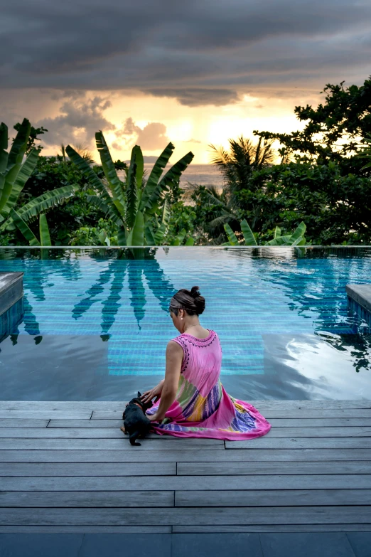 a woman sitting on the edge of a swimming pool, golden hour in boracay, lush surroundings, skies behind, dwell