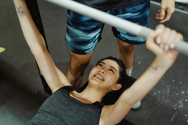 a woman lifting a bar in a gym, by Reuben Tam, pexels contest winner, smiling down from above, manuka, lachlan bailey, jen bartel