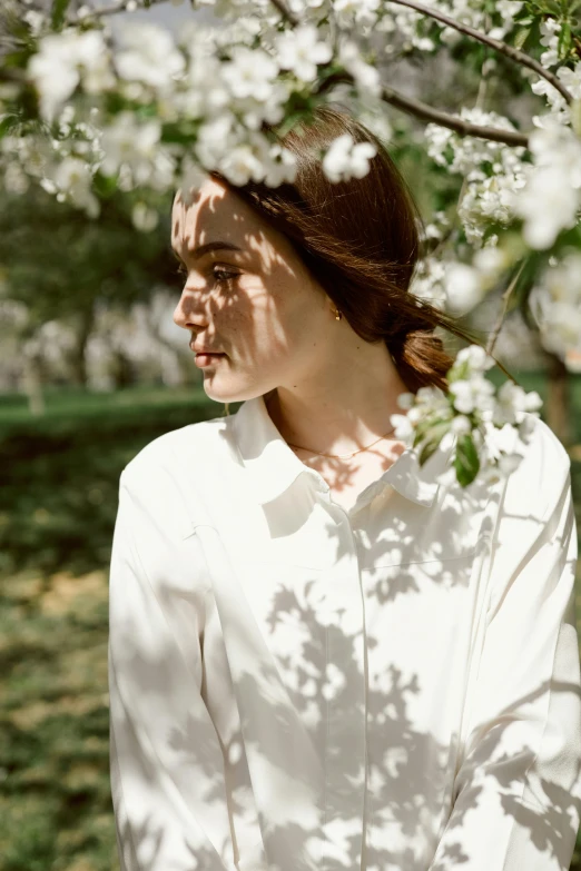 a woman in a white shirt standing under a tree, soft bloom lighting, wearing collar, wearing a linen shirt, ivory pale skin