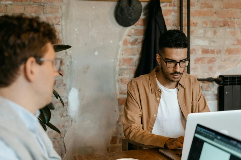 two men sitting at a table working on laptops, trending on pexels, gif, background image, ash thorp khyzyl saleem, man with glasses