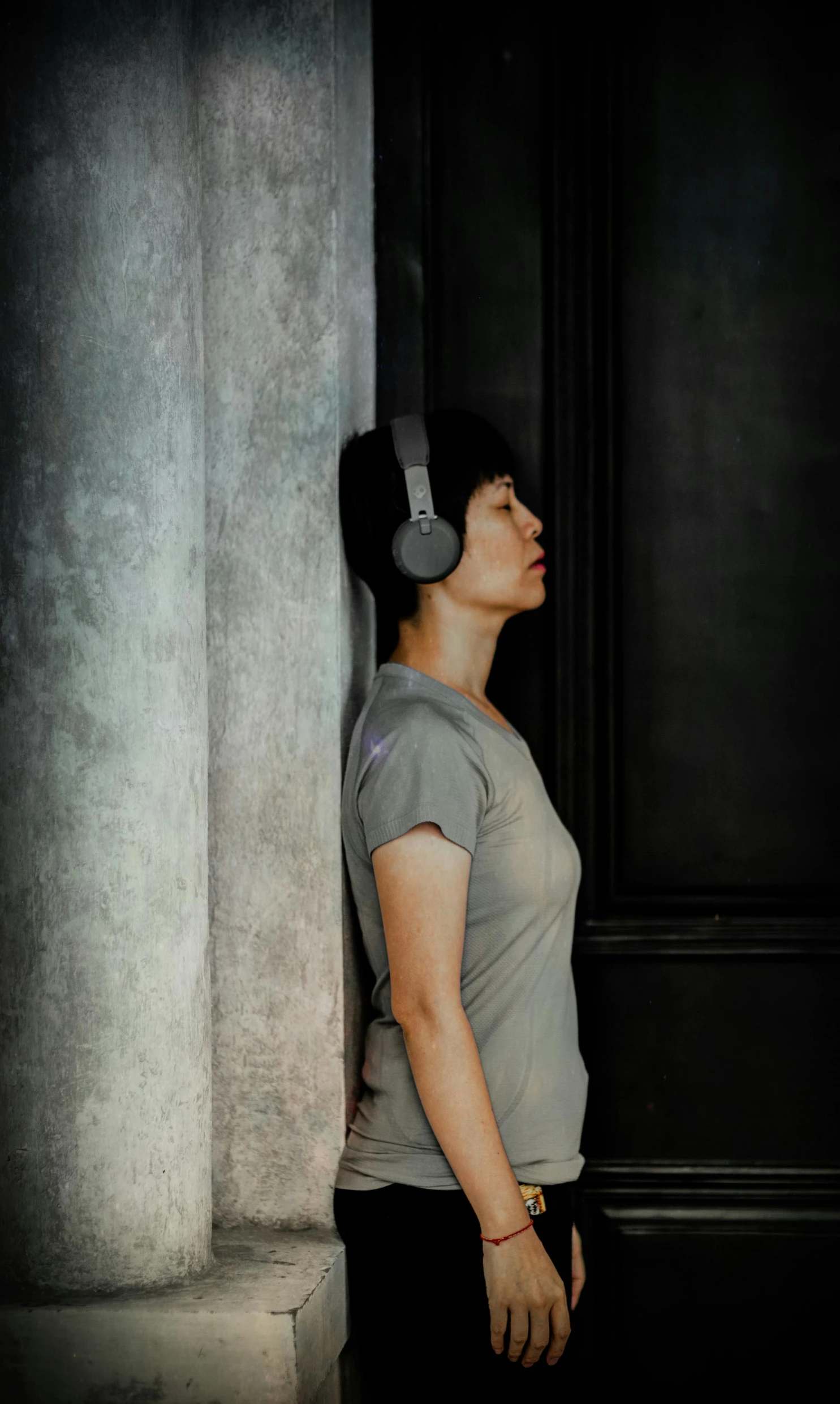 a woman leaning against a wall with headphones on, by Nina Hamnett, asian human, profile image, colin greenwood (bass), promotional image
