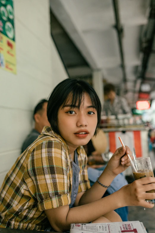 a woman sitting at a table with a drink in her hand, by Tan Ting-pho, pexels contest winner, portrait of teenage girl, square, jakarta, with short hair