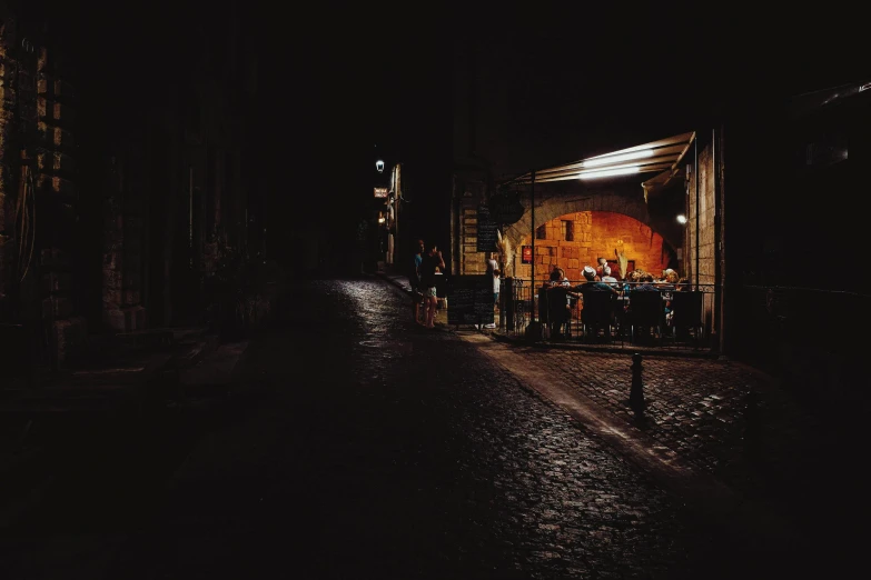 a group of people sitting at a table in the dark, an album cover, by Giuseppe Avanzi, pexels contest winner, cobblestone streets, slightly pixelated, distant photo, agrigento
