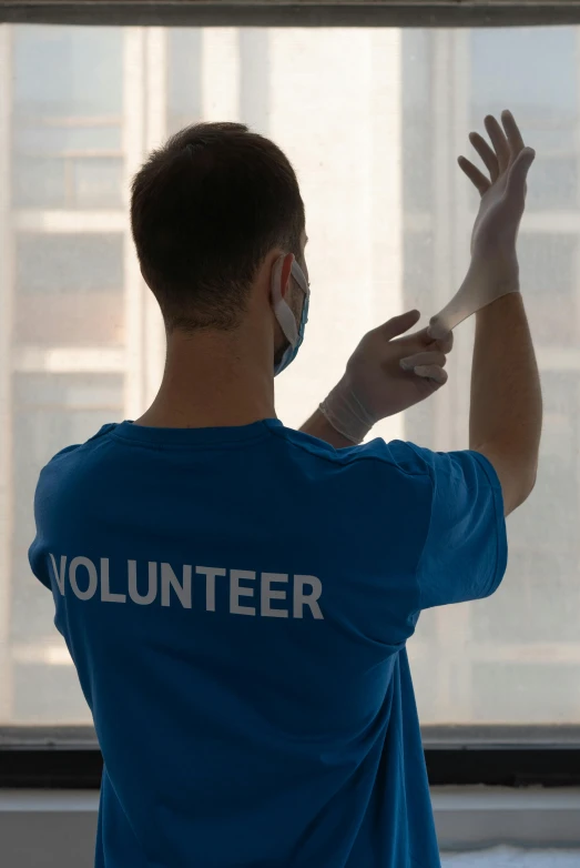 a man in a blue shirt standing in front of a window, by Francis Helps, shutterstock, graffiti, wearing gloves, united nations, promotional image, back lit