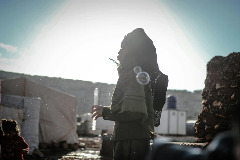 a woman standing next to a pile of garbage, a portrait, by Julia Pishtar, unsplash, hurufiyya, soldier with a gasmask, bubbles, islamic, harsh sunlight