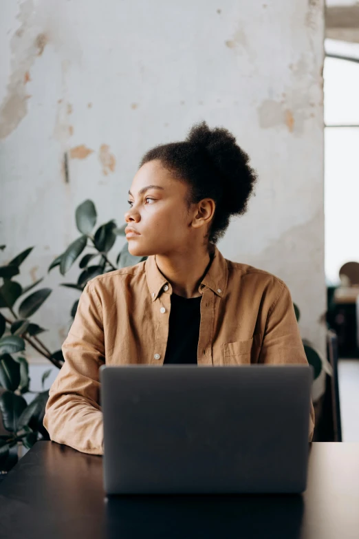 a woman sitting at a table with a laptop, a portrait, by Carey Morris, trending on unsplash, looking serious, afro tech, looking off into the distance, without text