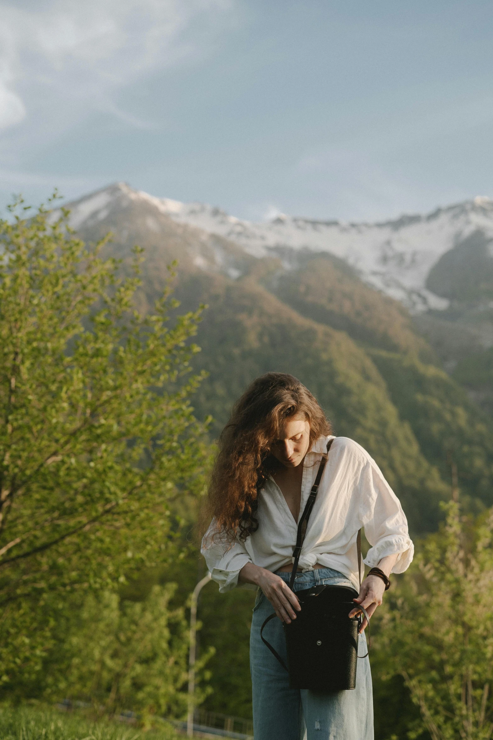 a woman standing on top of a lush green hillside, inspired by Elsa Bleda, trending on unsplash, renaissance, wearing a white button up shirt, snow capped mountains, fashion shoot 8k, medium format. soft light