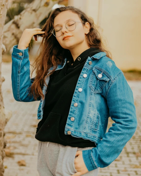 a woman standing next to a tree with her eyes closed, an album cover, inspired by Ion Andreescu, trending on unsplash, photorealism, denim jacket, lovingly looking at camera, spectacled, ((blue))