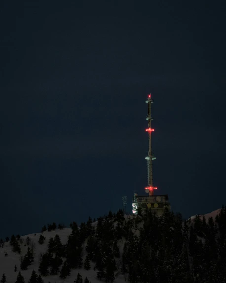 a tall tower sitting on top of a snow covered slope, red leds, antenna, out in the dark, black forest