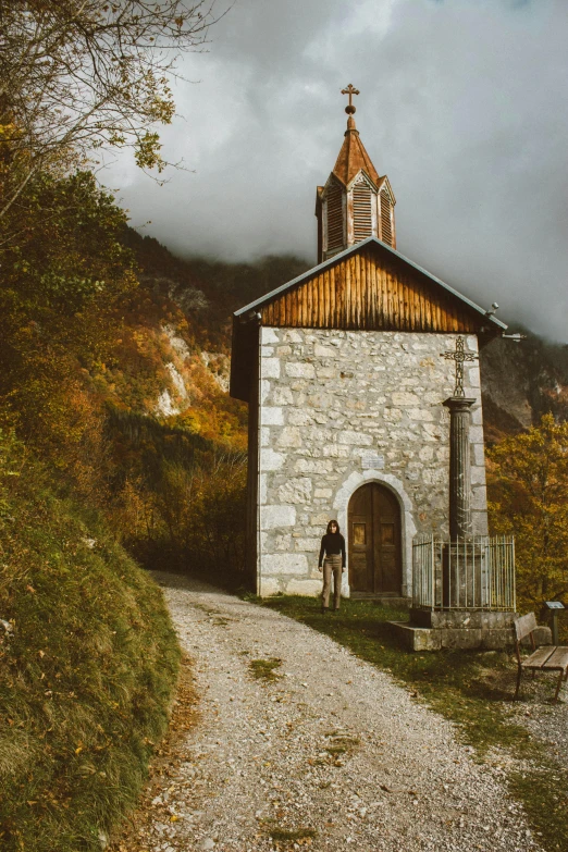 a small church sitting on the side of a road, pexels contest winner, romanesque, girl of the alps, vintage color, fall, standing in a grotto