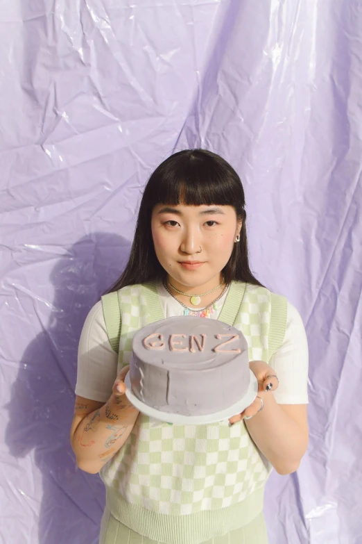 a woman holding a cake in front of a purple backdrop, an album cover, trending on pexels, yanjun chengt, grey, 2 people, headshot profile picture