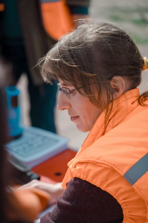 a woman in an orange vest working on a laptop, a photo, by Alison Watt, happening, cartographic, emergency, worksafe. cinematic, : :