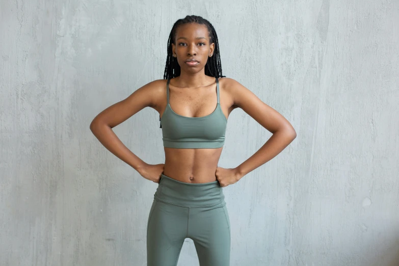 a woman standing with her hands on her hips, trending on pexels, sage green, sports bra, adut akech, olive skin color