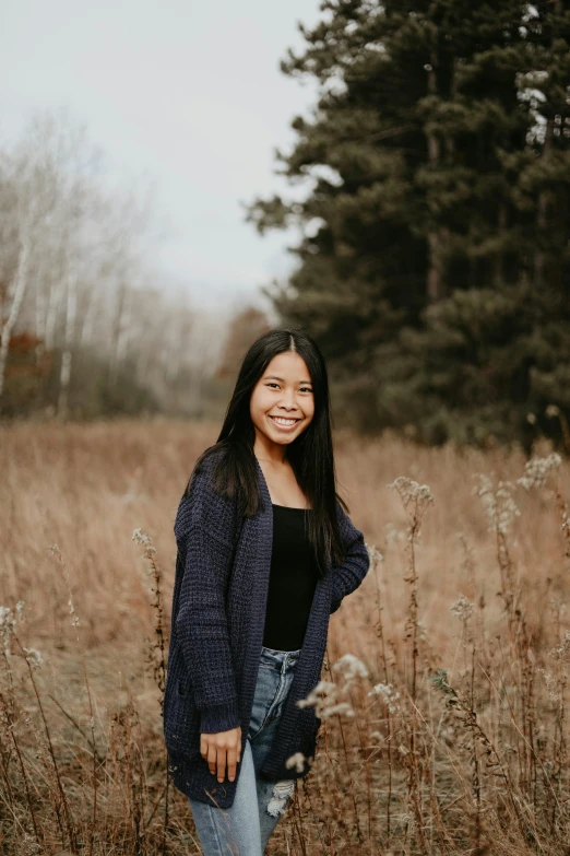 a woman standing in a field of tall grass, a picture, inspired by Ruth Jên, pexels contest winner, smiling girl, in a navy blue sweater, graduation photo, asian descent