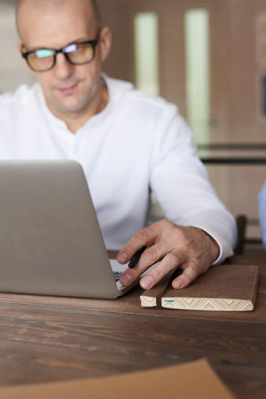 a man sitting at a table using a laptop computer, holding a wood piece, wood effect, expert design, multiple stories