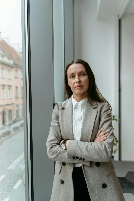 a woman standing in front of a window with her arms crossed, by Emma Andijewska, female lawyer, petri rahkola, looking serious, high quality photo