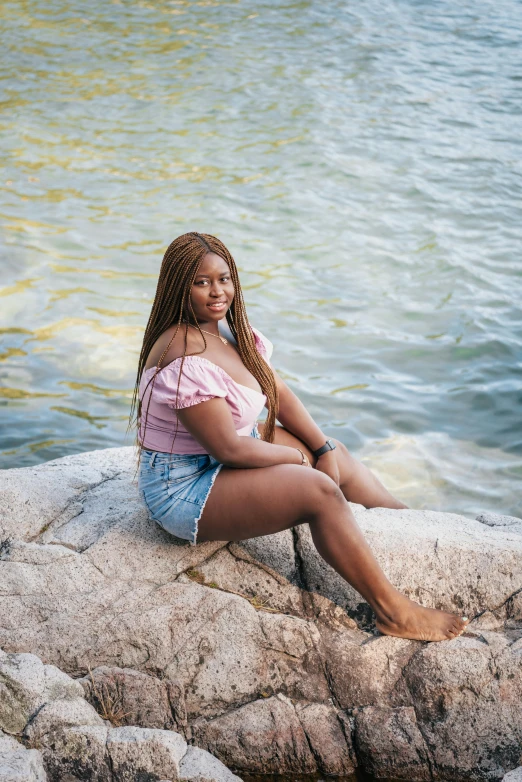 a woman sitting on a rock by the water, with brown skin, posing for a picture, thighs, african canadian