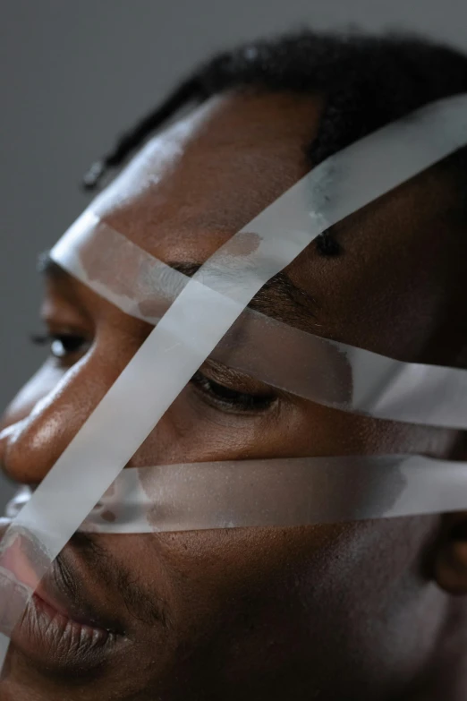 a close up of a person with tape on their face, pexels contest winner, afrofuturism, translucent material, white ribbon, light stubble, struggling