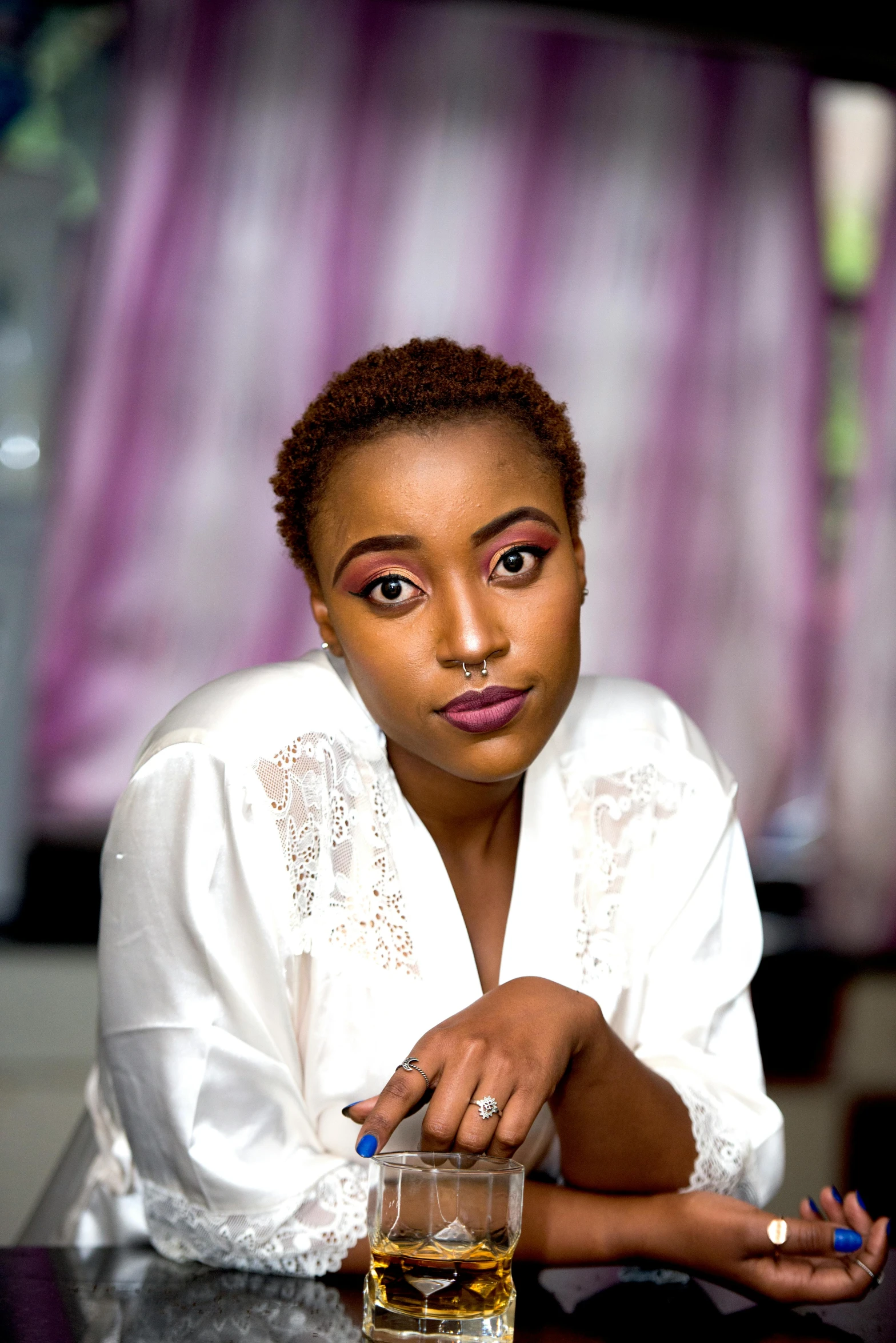 a woman sitting at a table with a glass of alcohol, an album cover, by Chinwe Chukwuogo-Roy, pexels contest winner, cute girl with short pink hair, wearing a white button up shirt, dramatic serious pose, brown skin. light makeup