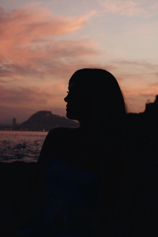 a woman sitting on top of a beach next to the ocean, inspired by Elsa Bleda, pexels contest winner, happening, rio de janeiro, silhouette :7, woman's face looking off camera, panoramic view of girl