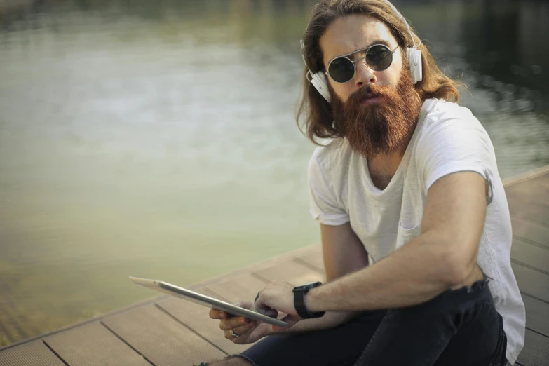 a man sitting on a dock using a tablet computer, an album cover, trending on pexels, reddish beard, nerds, : 5 stylish, ultra - realistic