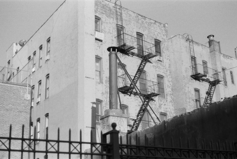 a black and white photo of a building with fire escapes, a black and white photo, ashcan school, color film still, rear view, lock, chimney