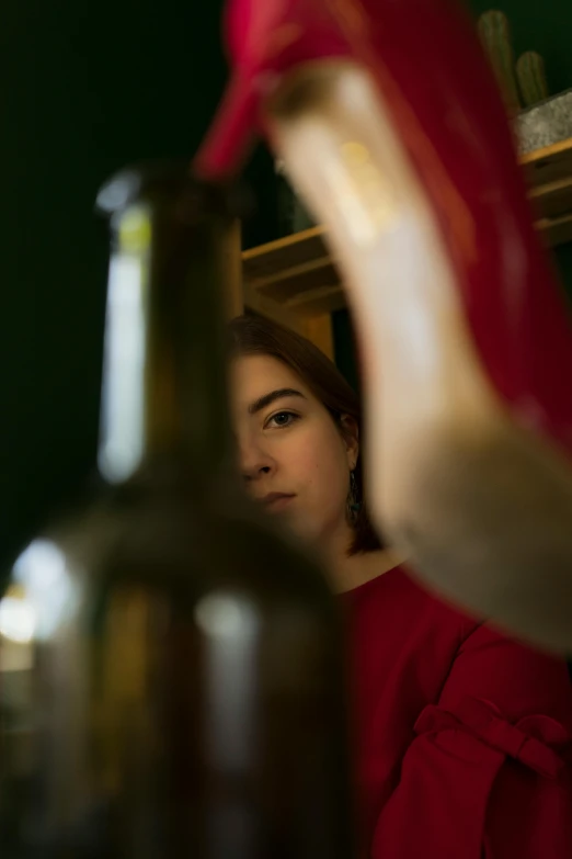 a woman standing in front of a bottle of wine, a portrait, inspired by Elsa Bleda, pexels contest winner, mirrors, olive green and venetian red, girl with warship parts, slightly out of focus