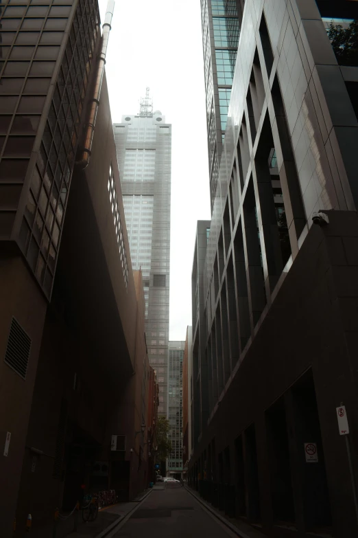 a narrow city street lined with tall buildings, inspired by Thomas Struth, melbourne, tall minimalist skyscrapers, dark and misty, distant - mid - shot