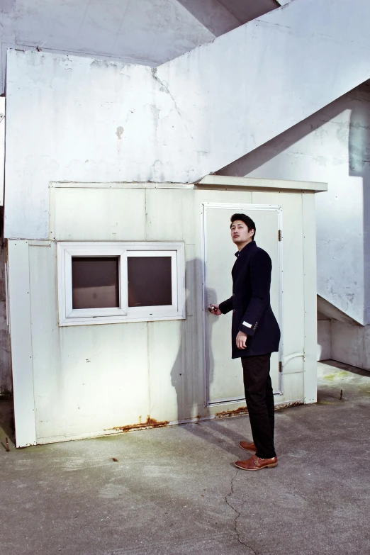 a man standing in front of a white building, an album cover, mark edward fischbach, standing in corner of room, model photograph, korean film noir