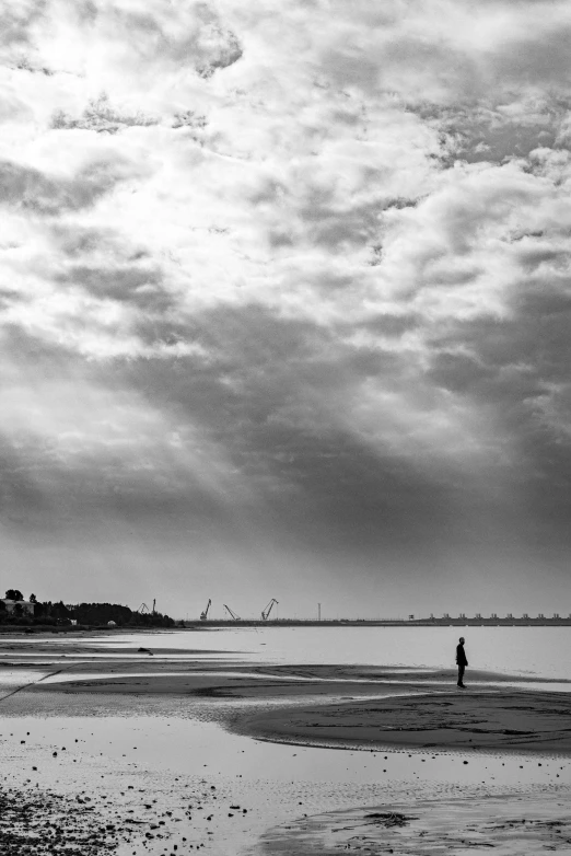 a person standing on a beach flying a kite, a black and white photo, by Altichiero, minimalism, harbour, crepuscular ray, distant city, cloud day