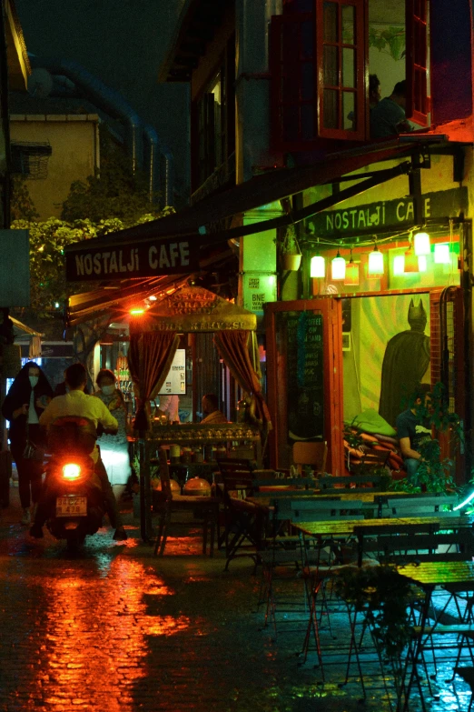 a group of people walking down a street at night, raining outside the cafe, istanbul, absinthe, vibrant scene