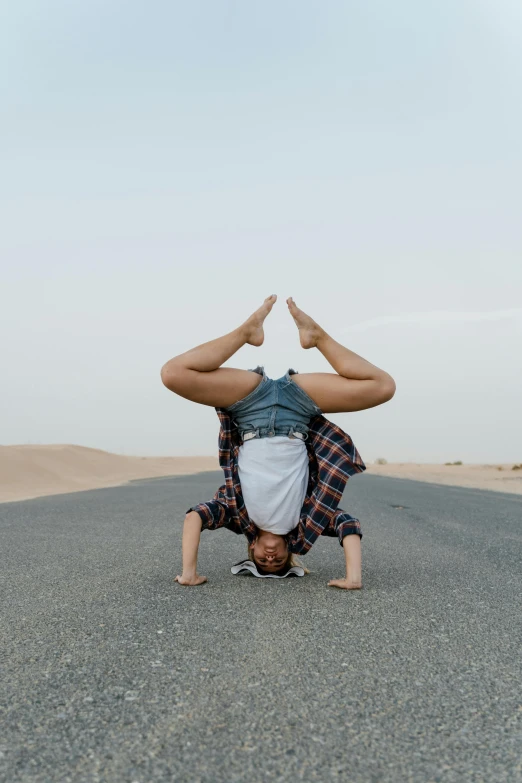 a man doing a handstand in the middle of the road, by Nina Hamnett, arabesque, arabian wrestling woman, profile image, in a desert, head tilted down