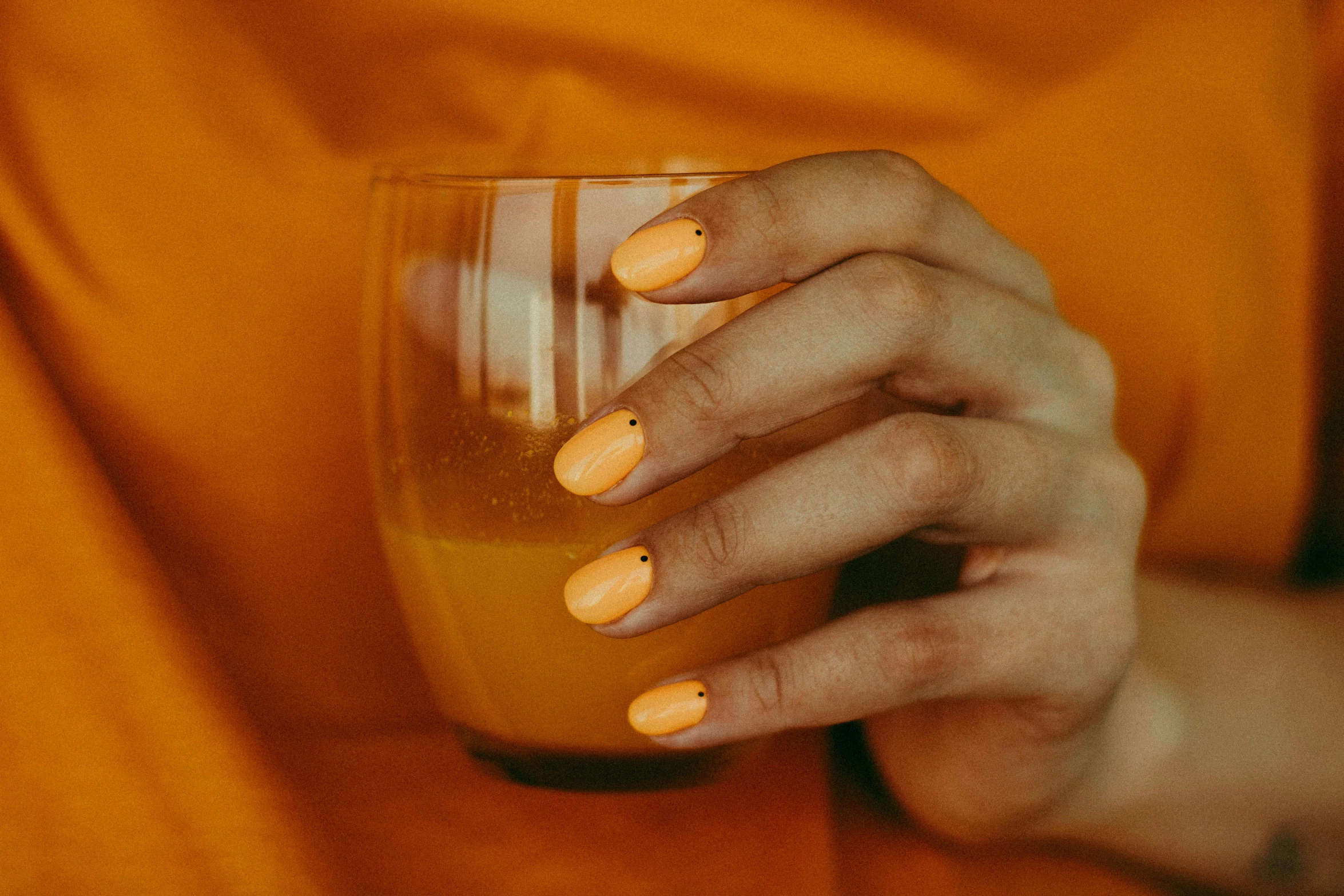 a woman holding a glass of orange juice, inspired by Elsa Bleda, trending on pexels, nail art, warm coloured, monochromatic, thumbnail