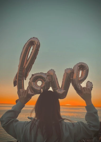 a woman holding up balloons in the shape of the word love, by Julia Pishtar, trending on unsplash, romanticism, instagram story, foil, teenager, 🚿🗝📝