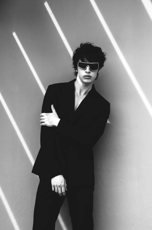 a man in a suit and sunglasses leaning against a wall, an album cover, inspired by Robert Mapplethorpe, tumblr, finn wolfhard, black and white), riccardo scamarcio, dressed in black velvet