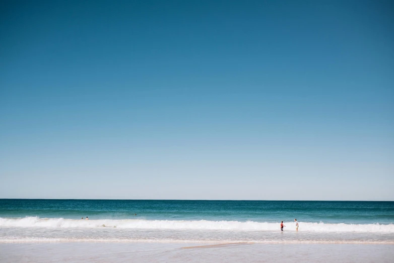 a person standing on a beach next to the ocean, unsplash contest winner, minimalism, on a hot australian day, people swimming, light blue clear sky, shot on hasselblad