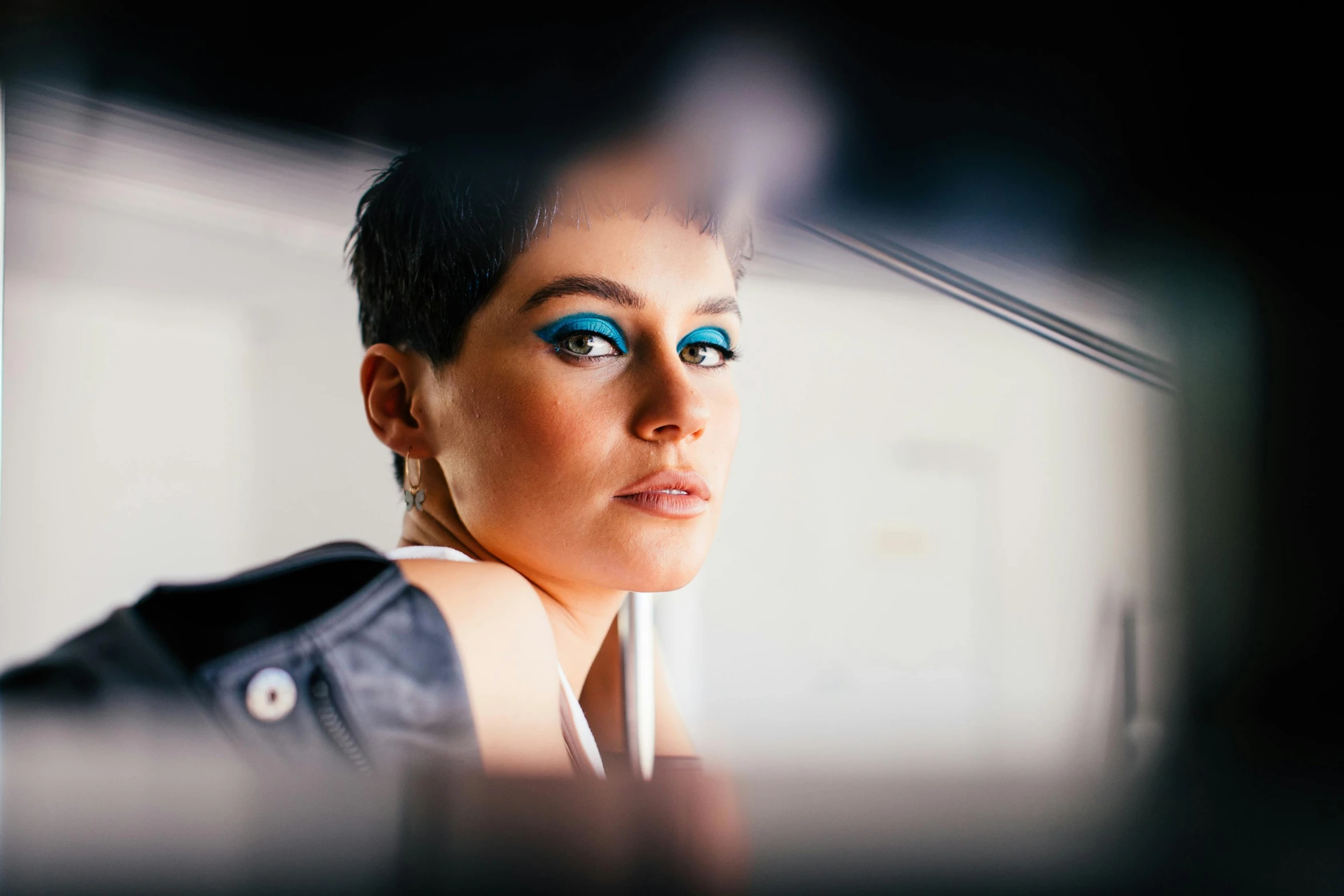 a woman looking at her reflection in a mirror, an album cover, inspired by Elsa Bleda, trending on pexels, short blue haired woman, bright blue eyes, with professional makeup, car shot