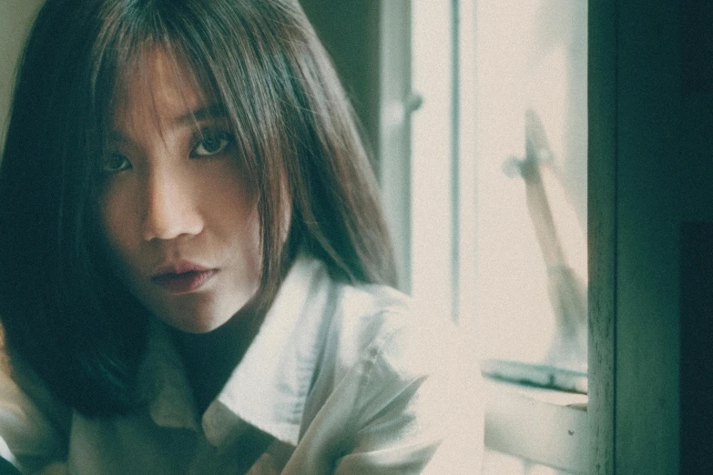 a woman in a white shirt leaning against a window, an album cover, inspired by Yu Zhiding, unsplash, gemma chan girl portrait, grainy footage, hsiao-ron, color graded