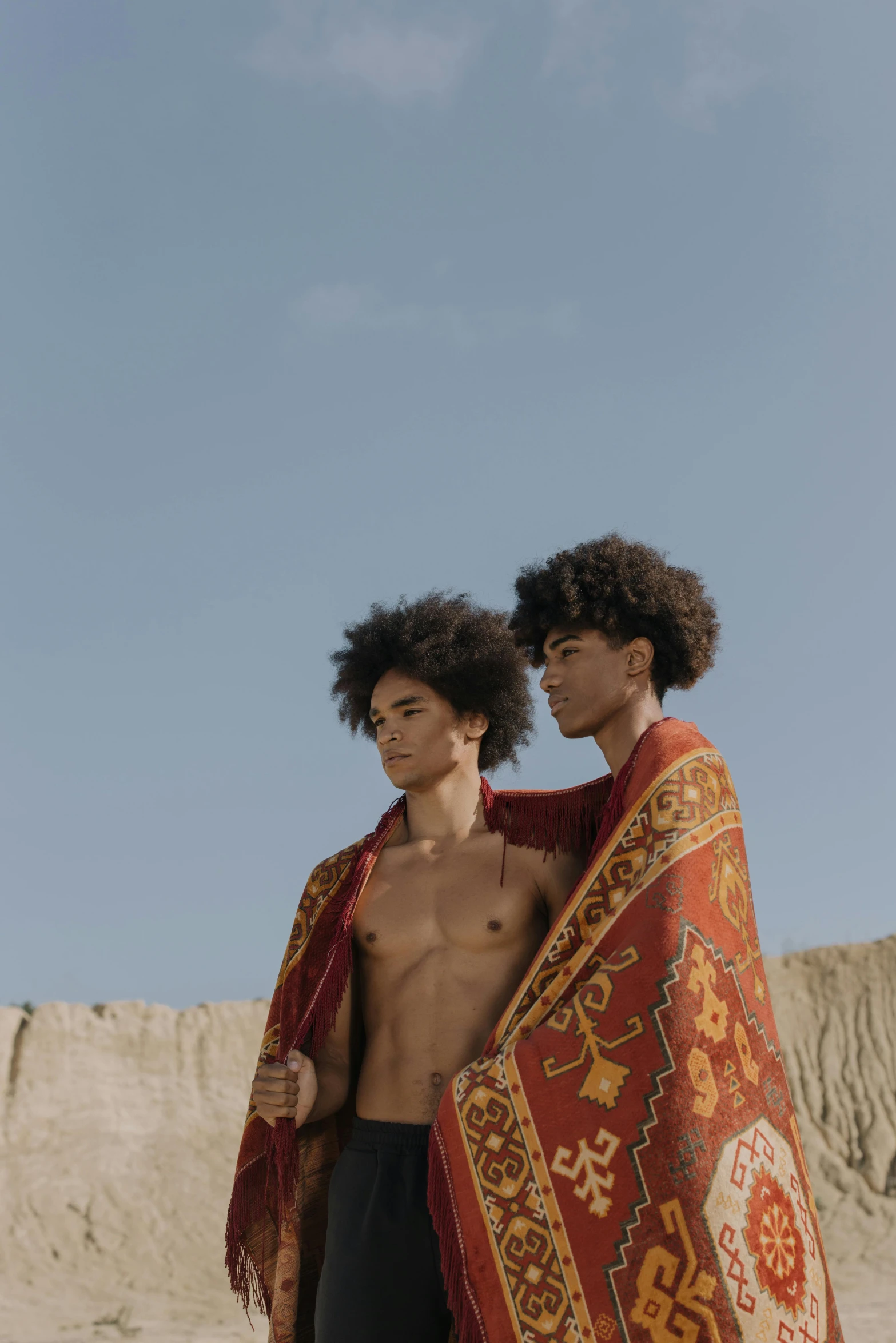 a couple of men standing on top of a sandy beach, by Nathalie Rattner, trending on pexels, afrofuturism, long afro hair, tapestry, disrobed, ( ( theatrical ) )