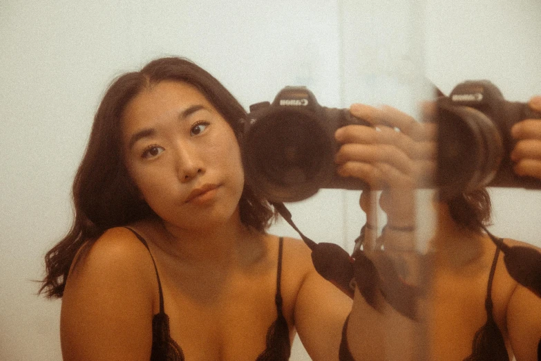 a woman taking a picture of herself in a mirror, inspired by Ren Hang, unsplash, photorealism, she is wearing a black tank top, taken in the early 2020s, lovingly looking at camera, half asian