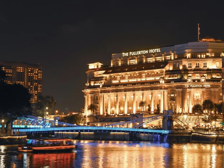 a large building sitting on top of a river next to a bridge, by Julia Pishtar, hotel room, at night, neo classical architecture, singapore esplanade