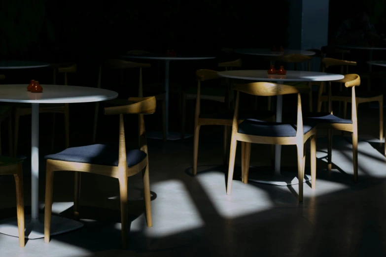 a number of tables and chairs in a room, pexels contest winner, light and space, shadowy lighting, sitting on a chair, table in front with a cup, light dark