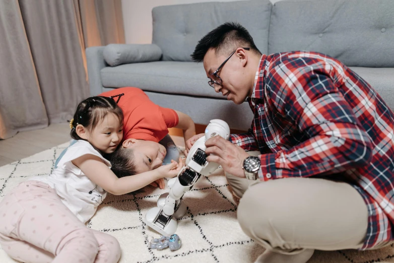 a man playing with two children on the floor, inspired by Leo Leuppi, pexels contest winner, with a robotic arm, avatar image, asian human, high quality image