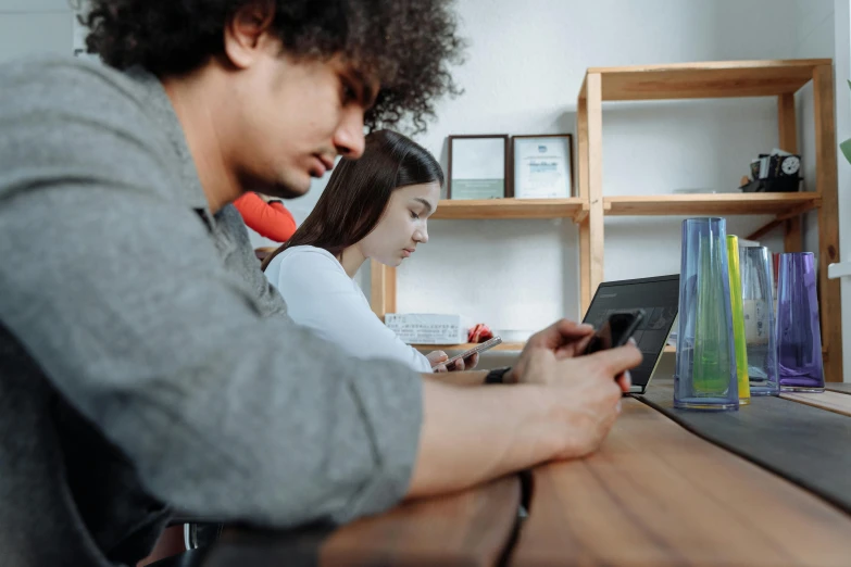 a couple of people sitting at a table with a laptop, a picture, trending on pexels, pixel art, taken on iphone 14 pro, gaming, in a classroom, realistic »