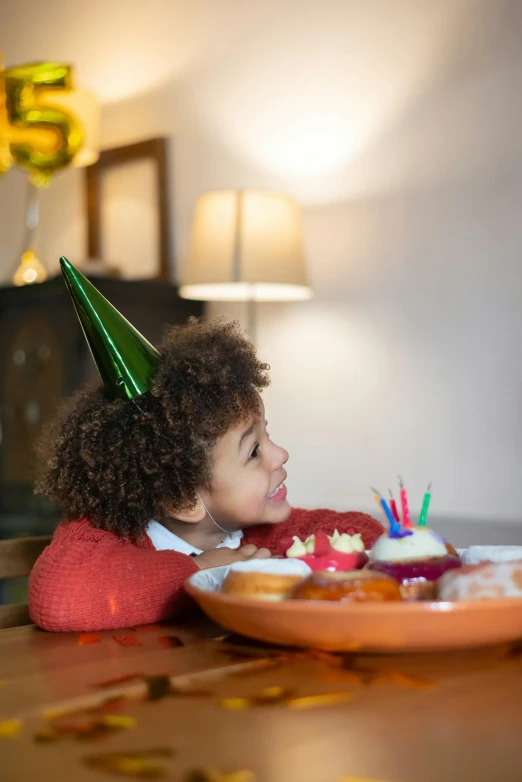 a little girl sitting at a table with a plate of cake, pexels, wearing a party hat, little elf tomboy, african american girl, a cozy